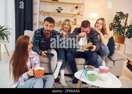 Playing video game. Group of friends have party indoors together. Stock Photo