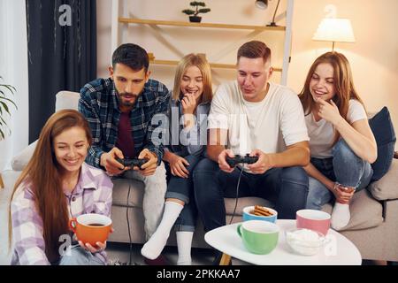 Using joysticks to play video game. Group of friends have party indoors together. Stock Photo