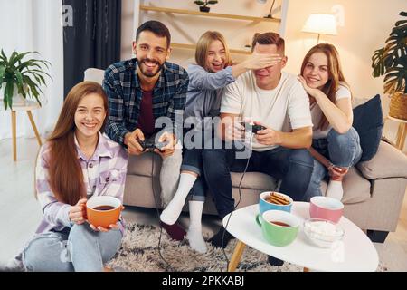 Using joysticks to play video game. Group of friends have party indoors together. Stock Photo