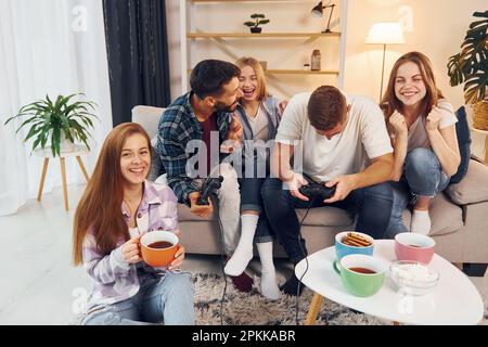 Using joysticks to play video game. Group of friends have party indoors together. Stock Photo