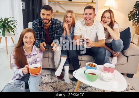 Using joysticks to play video game. Group of friends have party indoors together. Stock Photo