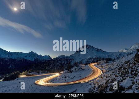 Lights of car trails on winding road covered with snow at night, Bernina Pass, Val Poschiavo, Graubunden canton, Switzerland, Europe Stock Photo