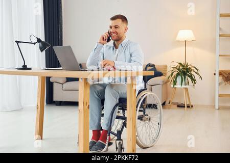 Using laptop. Disabled man in wheelchair is at home. Stock Photo