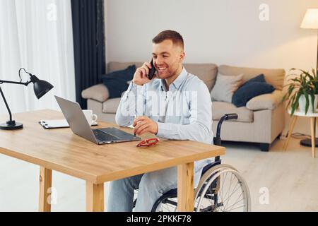 Using laptop. Disabled man in wheelchair is at home. Stock Photo