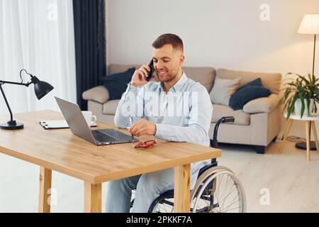 Using laptop. Disabled man in wheelchair is at home. Stock Photo