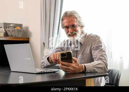 Senior grandfather using laptop and smart phone at home Stock Photo