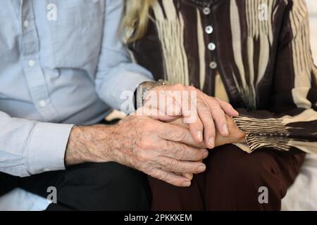 Close up hands of elderly couple holding hands while sitting at home Stock Photo