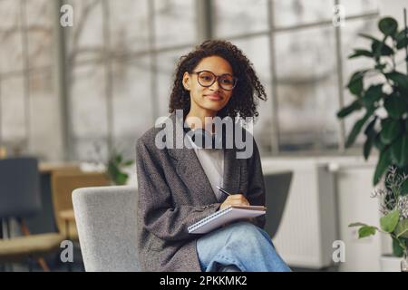Young woman student in headphones making notes in a notebook in the modern coworking Stock Photo