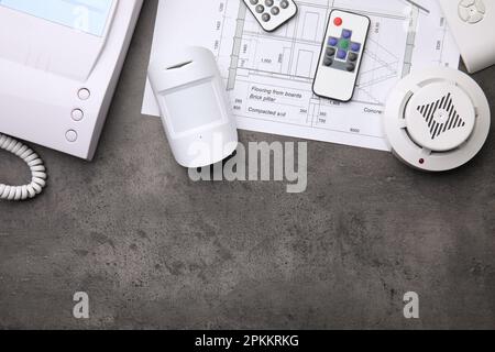Building plan, remote controls, smoke and movement detectors on grey table, flat lay with space for text. Home security system Stock Photo