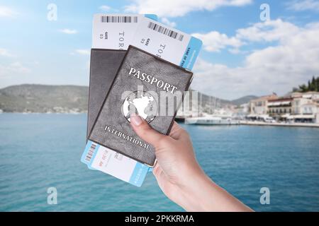 Woman holding international passports with boarding passes and beautiful view of boats in sea near shore on background Stock Photo