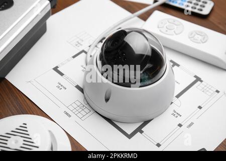 CCTV camera and building plan on wooden table, closeup. Home security system Stock Photo