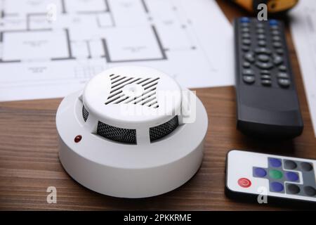Smoke detector and remote controls on wooden table, closeup. Home security system Stock Photo