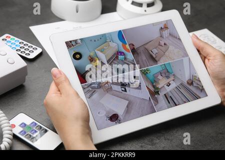 Woman monitoring CCTV cameras on tablet at grey table, closeup. Home security system Stock Photo