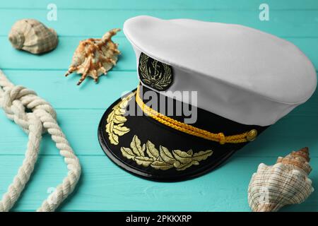Peaked cap, rope and shells on turquoise wooden background Stock Photo