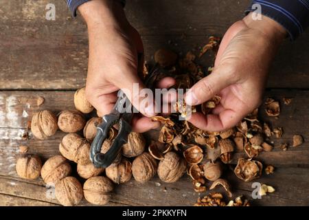 Man cracking walnuts at wooden table, closeup Stock Photo