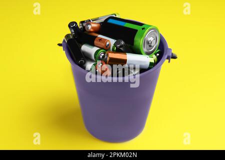 Used batteries in bucket on yellow background, closeup Stock Photo