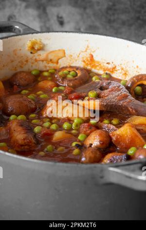 Sausage casserole in a red casserole dish, with potato, mushrooms, tomatoes, peas and onion, in a beef stock. Stock Photo