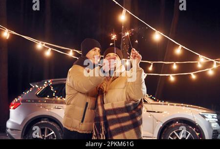 Holding sparklers. Couple standing in the forest and celebrating New year. Stock Photo