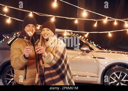 Holding sparklers. Couple standing in the forest and celebrating New year. Stock Photo