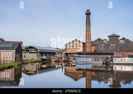 Narrow boats moored around the pump house at Ellesmere Port on the Ellesmere Canal reflect in the water in April 2023. Stock Photo