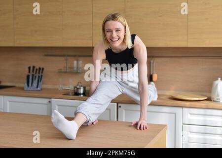 Woman doing the splits in kitchen between tables. Stock Photo