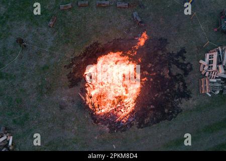Niederdorfelden, Germany. 08th Apr, 2023. A reservist sprays water on the fire during an Easter bonfire organized by the Reservistenkameradschaft Kinzigtal and the Teufelskappen e.V. association. (Aerial view with drone) Credit: Sebastian Gollnow/dpa/Alamy Live News Stock Photo