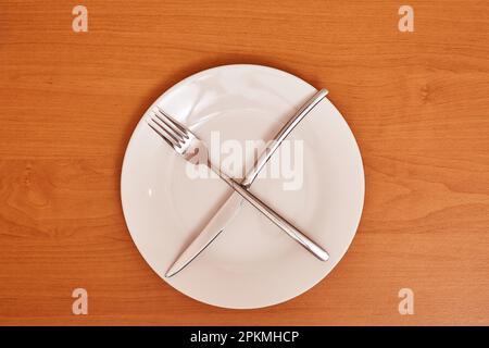 A signal 'I'm waiting for the next meal'. Empty and clean blue plate with fork and knife on a wooden table as an example of table etiquette Stock Photo