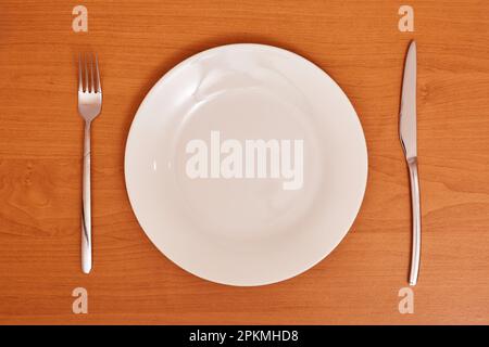 Empty and clean blue plate with fork and knife on a wooden table as an example of table etiquette Stock Photo