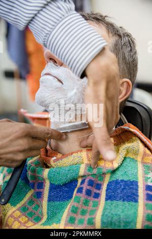 An American tourist getting a straight razor shave at a barbershop in Marrakech Morocco Stock Photo