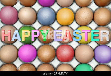 Colored, brown eggs in egg carton with letters "Happy Easter" in front. Stock Photo
