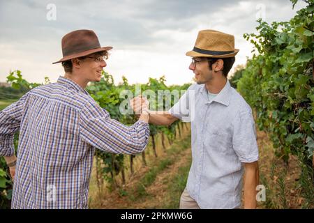 Two farmers shake hands and are happy as they stand in the vineyard. Stock Photo