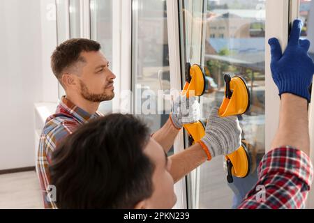 Workers using suction lifters during plastic window installation indoors Stock Photo