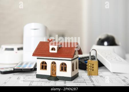 House model, CCTV camera, lock, remote controls, smoke and movement detectors on building plan. Home security system Stock Photo