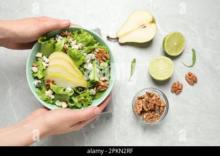 Woman holding tasty salad with pear slices at light grey marble table, top view Stock Photo