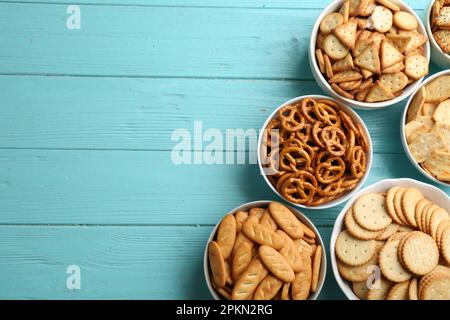 Different delicious crackers in bowls on turquoise wooden table, flat lay. Space for text Stock Photo