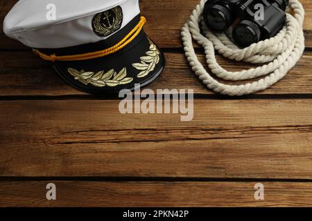 Peaked cap and rope with binoculars on wooden background, space for text Stock Photo