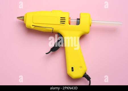 Yellow glue gun with stick on pink background, top view Stock Photo