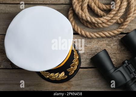 Peaked cap, rope and binoculars on wooden background, flat lay Stock Photo