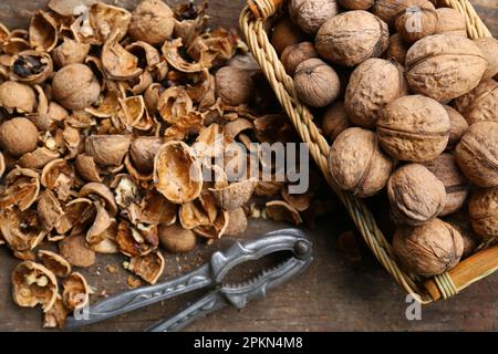 Walnuts, pieces of shells and nutcracker on wooden table, flat lay Stock Photo