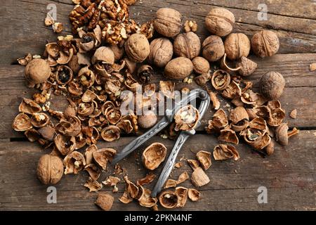 Walnuts, pieces of shells and nutcracker on wooden table, flat lay Stock Photo