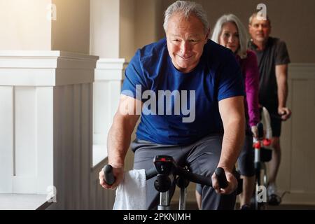 Smile through the pain and it will get better. a group of seniors having a spinning class at the gym. Stock Photo