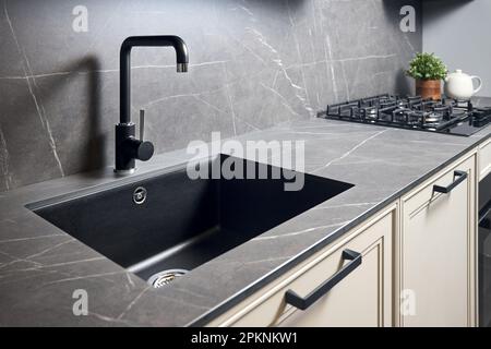 Kitchen sink area with black square matte sink tap in contemporary style. Matte black and stoneware kitchen design. Black ceramic sink with gas hob Stock Photo