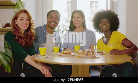 Multiethnic friends smiling at camera while eating breakfast at home Stock Photo