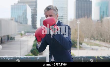 Mature businessman with boxing gloves in guard position outdoors Stock Photo