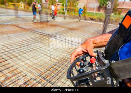 Operator, worker is holding industrial remote, wireless, console control with joystick to directing pump tube on right direction, pouring layer of con Stock Photo