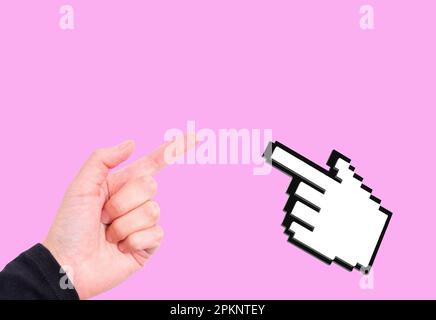 Human hand with pointing finger gesturing and blocky computer mouse hand cursor isolated on pink background with copy space. Stock Photo