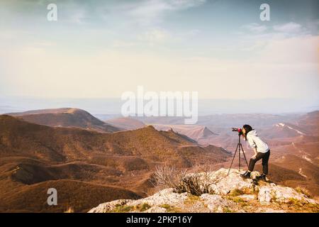 Young passionate attractive caucasian hipster woman content creator photographing mountains with red girly DSLR camera on tripod Stock Photo
