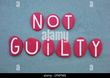 Not Guilty text composed with hand painted red colored stone letters over green sand Stock Photo