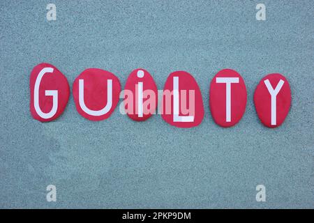 Guilty word composed with hand painted red hand painted stone letters over green sand Stock Photo