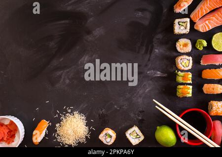Overhead shot of sushi and ingredients on dark background. Sushi rolls, nigiri, raw salmon steak, rice, cream cheese, avocado, lime, pickled ginger (g Stock Photo